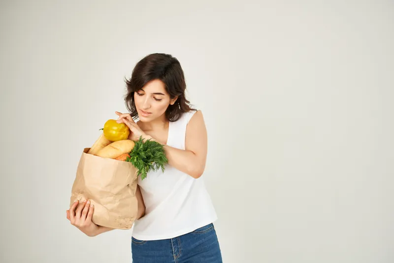 Весёлая брюнетка с пакетом продуктов и овощами в супермаркете, крупный план