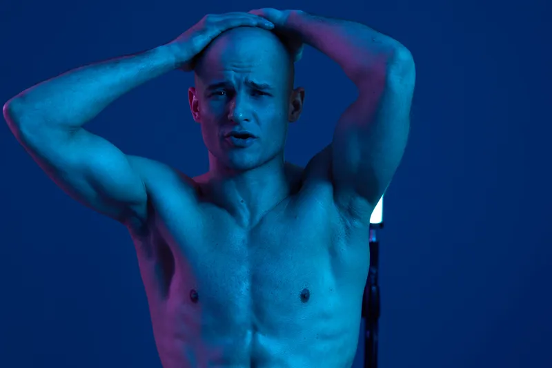 A man in dramatic lighting struggles with emotions, showcasing raw vulnerability and strength. The interplay of colors creates an intense atmosphere, emphasizing his expression.