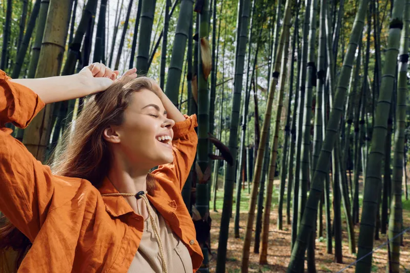 Woman smile bamboo forest nature outdoor happy portrait of a young woman enjoying sunlight and fresh air in a serene bamboo grove, relaxed expression and casual jacket lifestyle scene