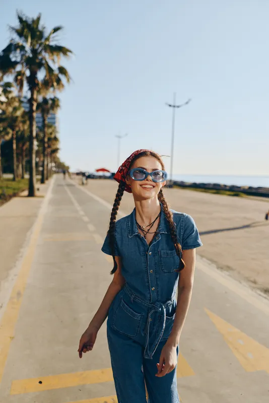 lifestyle woman in modern boho-western denim street style wearing sunglasses and red bandana, smiling outdoors with film color effect and sunny coastal background