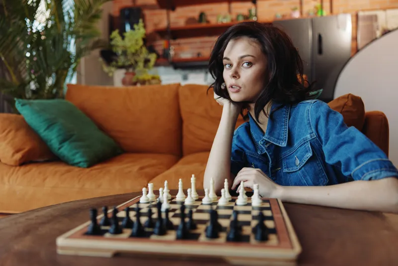 Женщина играет в шахматы, сидя на диване