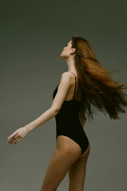 slender woman in black swimsuit with flowing hair on gray background