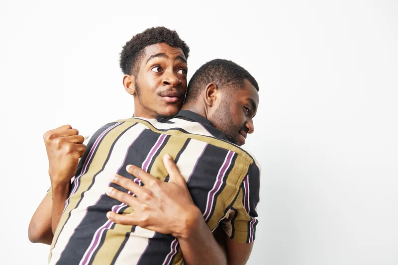Two black men embracing joyfully, showcasing friendship and warmth in a vibrant moment together. Their playful expressions reflect a strong bond and camaraderie.