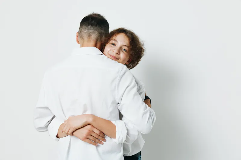 A professional man and colleague share a warm hug on a clean white background, conveying trust, teamwork, and confident emotion in a business setting.