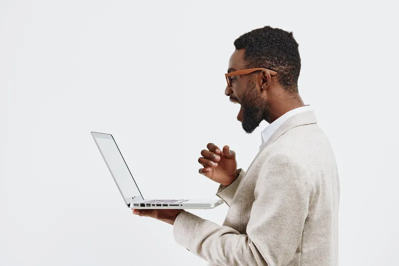 Smiling man using laptop computer, holding device in hand, dressed in beige blazer, glasses, casual office outfit, isolated on white background, modern technology, positive mood, professional concept