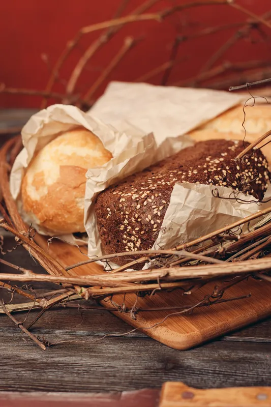 Буханка свежего хлеба, мука и продукт в птичьем гнезде на деревянном столе на красном фоне