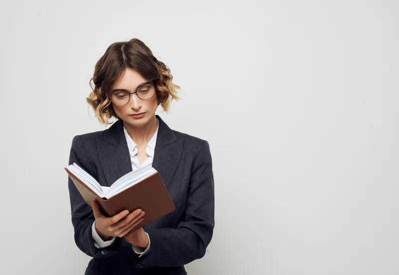 Женщина в деловом костюме с книгой в руках на светлом фоне