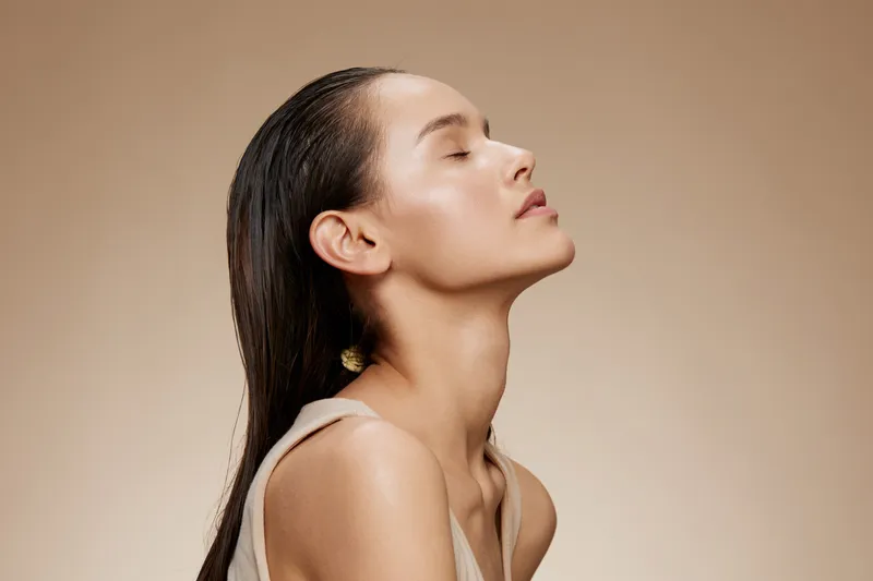 Serene young woman with wet hair and natural makeup, exuding calmness against a soft beige background, ideal for wellness or beauty concepts