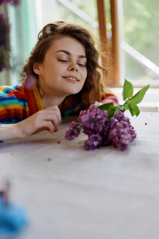 Relaxed woman admiring a bouquet on a bright indoor table, showcasing calm home lifestyle and self care. Soft natural light creates a warm, cozy atmosphere. For daily wellness at home.