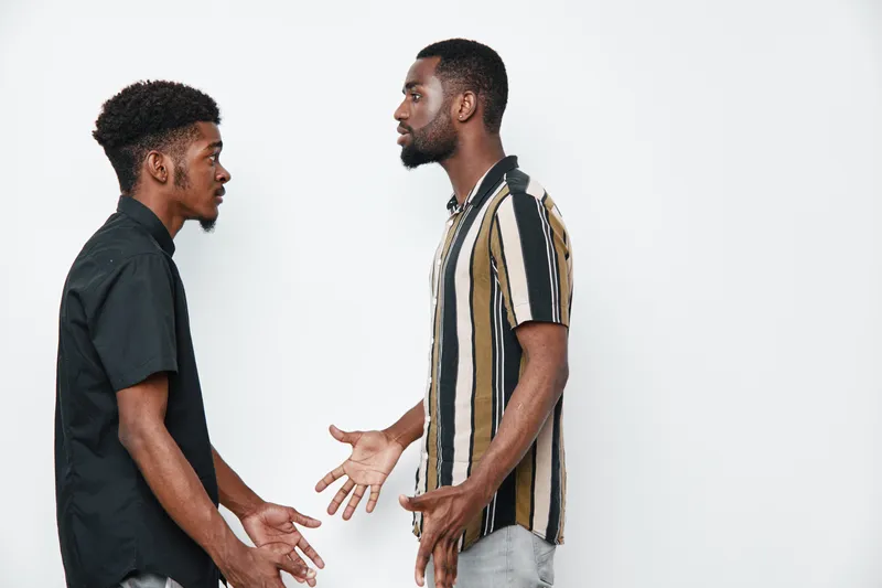 Two african american men with dark skin having serious conversation in casual clothes on white background. Young black males discussing with expressive gestures indoors.