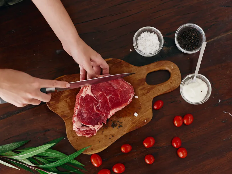 Женщина с ножом в руке нарезает свежее стейковое мясо для запекания на кухне