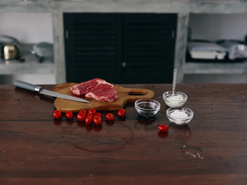 Женщина с ножом в руке режет стейк из мяса для жарки на кухне