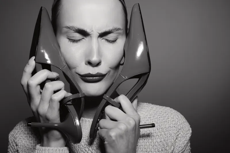 Close-up of a young white woman with pale skin holding high heel shoes to her face with closed eyes. Concept of fashion, style, and emotion.