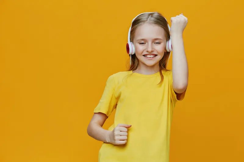 Joyful girl in yellow shirt dancing with headphones on a vibrant yellow background, expressing happiness and music enjoyment