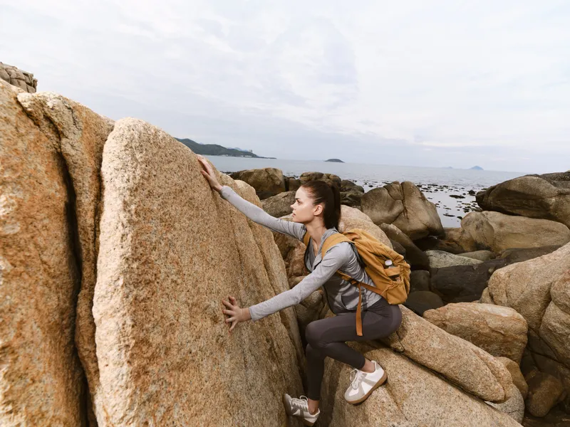 Adventurous young woman climber with a backpack exploring rocky coastline, embracing nature and enjoying outdoor activities