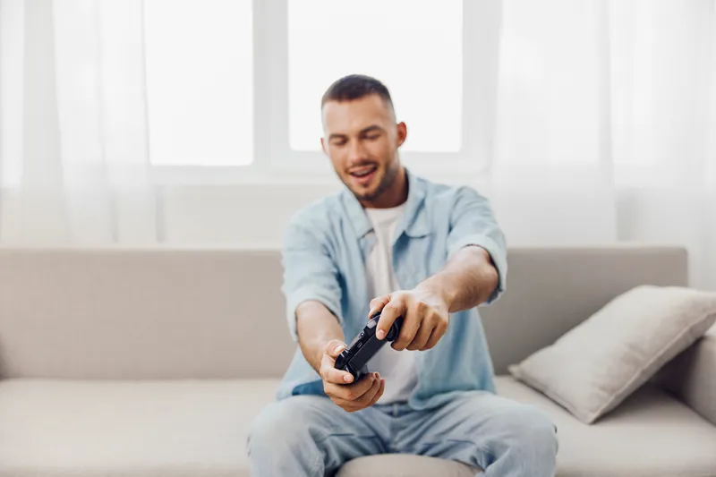 Engaged man playing video games, showcasing excitement and joy in a cozy living room atmosphere filled with natural light. Perfect for gaming culture themes.