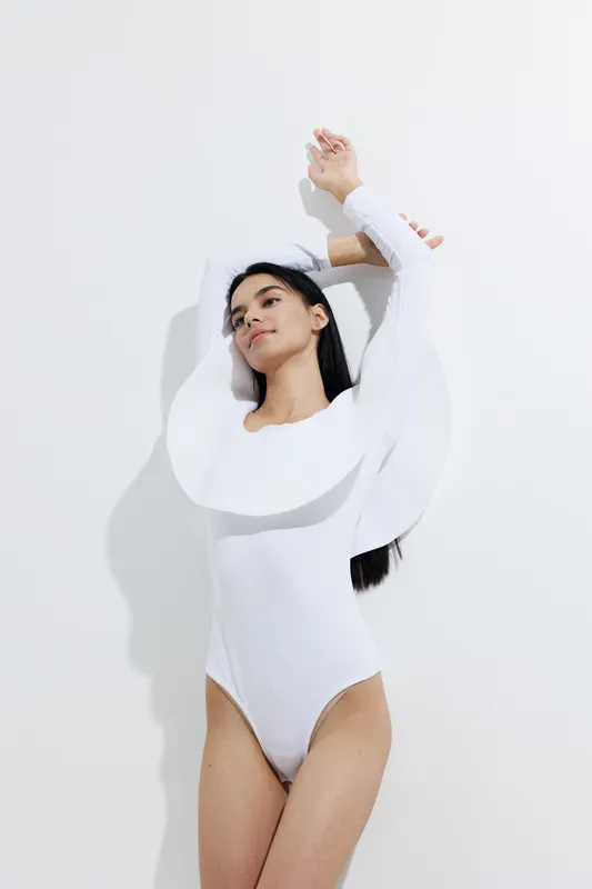 woman sport fitness wearing white bodysuit stretching gracefully against a plain white background with soft natural lighting
