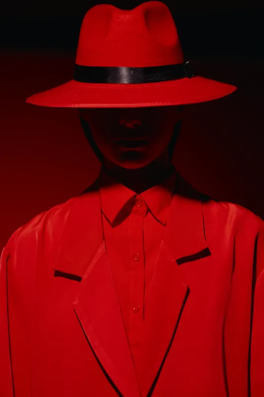 Stylish woman wearing red fedora and matching blazer, vibrant monochrome fashion photo with dramatic lighting and shadows, concept of bold beauty and creative style.