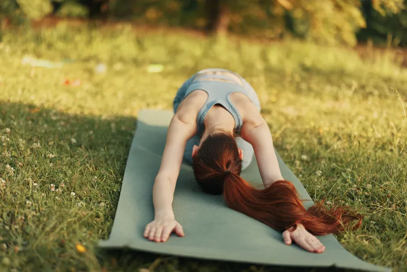 Peaceful young woman practicing yoga outdoors in a serene green setting, experiencing tranquility and harmony through deep stretching and relaxation