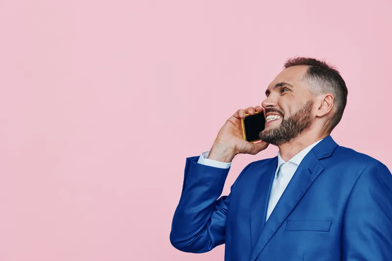 Professional business man on a pink isolated background, speaking on a mobile phone, radiating confidence and friendly energy, polished appearance and focused demeanor.