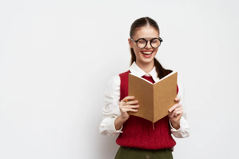 Счастливая студентка наслаждается чтением книги, стоя у белой стены