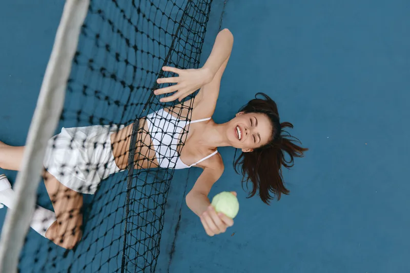 Cheerful young woman playing tennis, wearing sporty attire on a blue court, showcasing joy and energy, perfect for sports and fitness themes