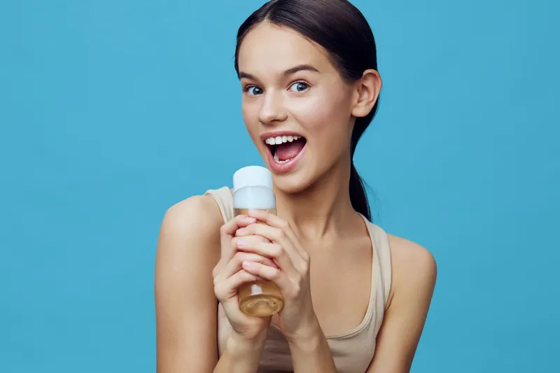 Happy young woman holding a healthy smoothie bottle against a vibrant blue background, showcasing a healthy lifestyle and vibrant energy