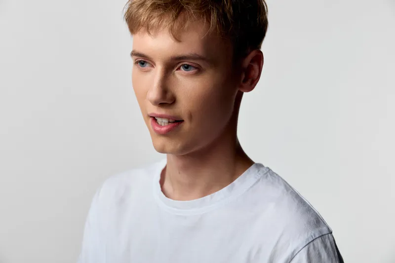 Young man, white shirt, casual style under studio lighting with a relaxed expression, suitable for fashion, lifestyle and stock photography in a clean minimalist studio for advertising and editorial