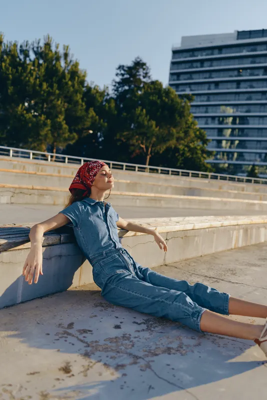 Lifestyle woman in modern boho-western denim street style relaxing outdoors with film color effect, enjoying sunny day and urban environment in casual outfit.