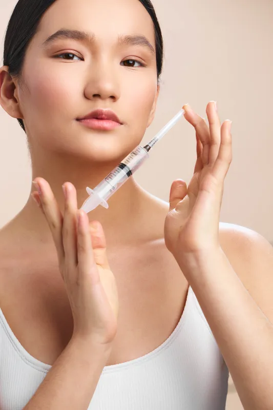 asian woman is seen preparing an injection in a clinical setting, calm and focused, displaying careful technique and professional care while handling the syringe.
