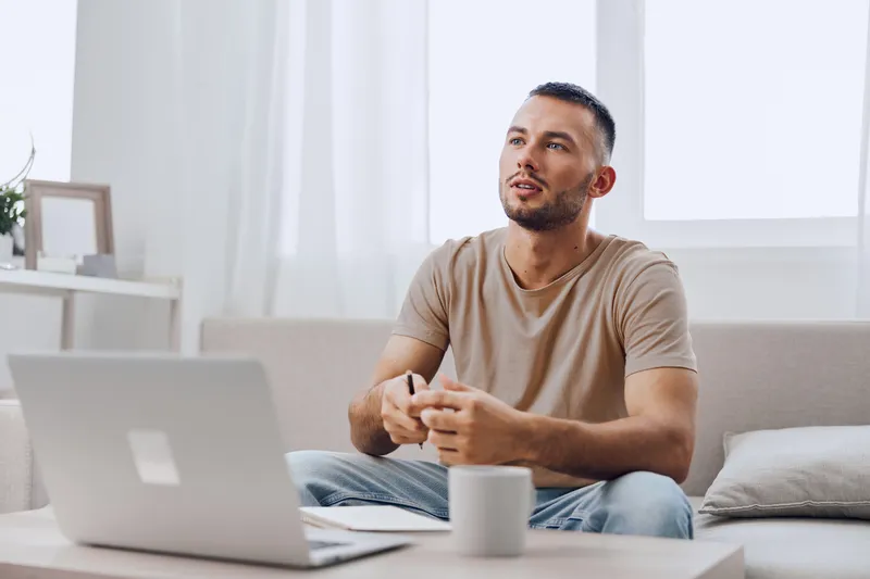 Thoughtful man engaged in a creative brainstorming session at home, surrounded by natural light and minimalist decor, emphasizing relaxation and productivity.