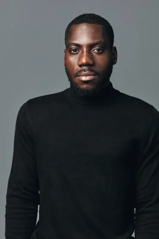 African man portrait with beard wearing black turtleneck sweater in creative conceptual visual style. Serious expression, studio lighting and neutral background for modern fashion look.