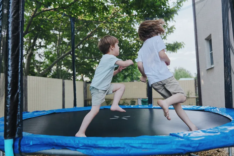 Playful children jumping on a trampoline, enjoying outdoor fun with laughter and excitement in a sunny backyard setting.