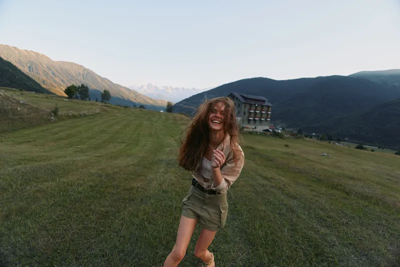 Happy woman outdoors running on grassy field with mountains in background smiling carefree natural light casual outfit summer day