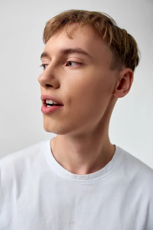 Young man in a white t shirt with a thoughtful sideways gaze, casual style, clean lighting and soft shadows, modern minimal vibe highlighting facial features and subtle expression suitable for