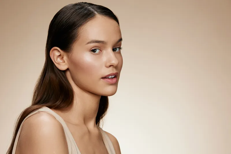 Young woman with natural makeup, showcasing healthy skin in a minimalist portrait with a neutral background and warm tones, emphasizing beauty and confidence
