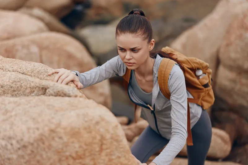 A determined young woman climbing rocky terrain, showcasing her athletic spirit in a gray outfit against a natural backdrop