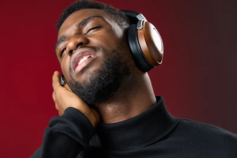 A young Black man enjoying music with headphones on, exuding relaxation and joy, set against a rich red background