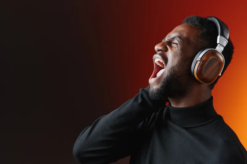 Young Black man listening to music with headphones, expressing joy and energy in a vibrant orange and black background, capturing the essence of music enjoyment