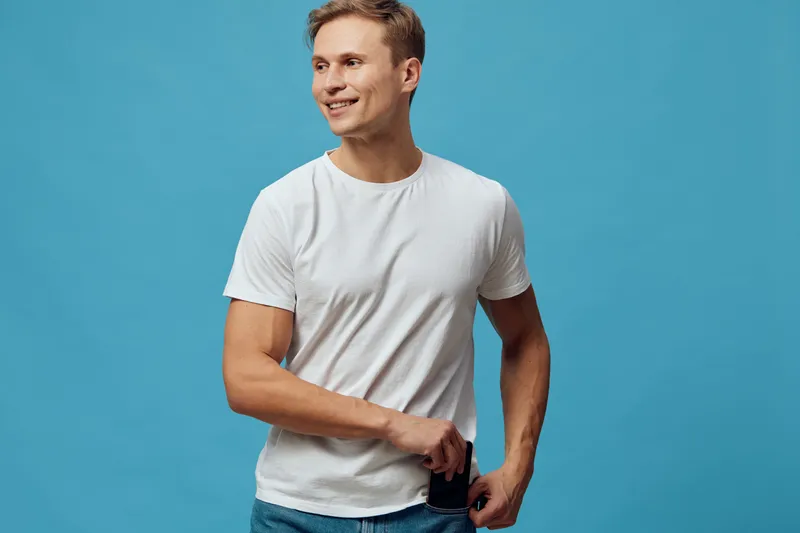 Smiling young man with short hair wearing casual white t-shirt and jeans, standing against a solid light blue background, relaxed pose, cheerful expression, casual style, lifestyle concept, isolated o