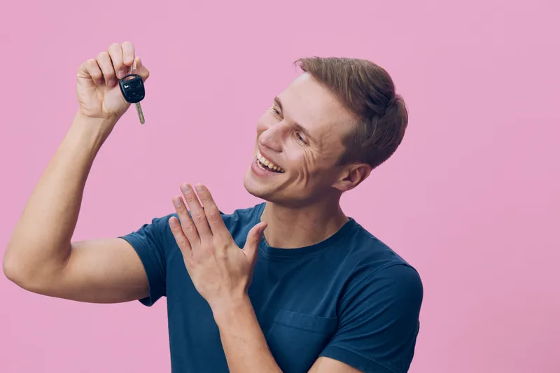 smiling man holding car key excited happy casual wear blue t-shirt pink background technology concept joy