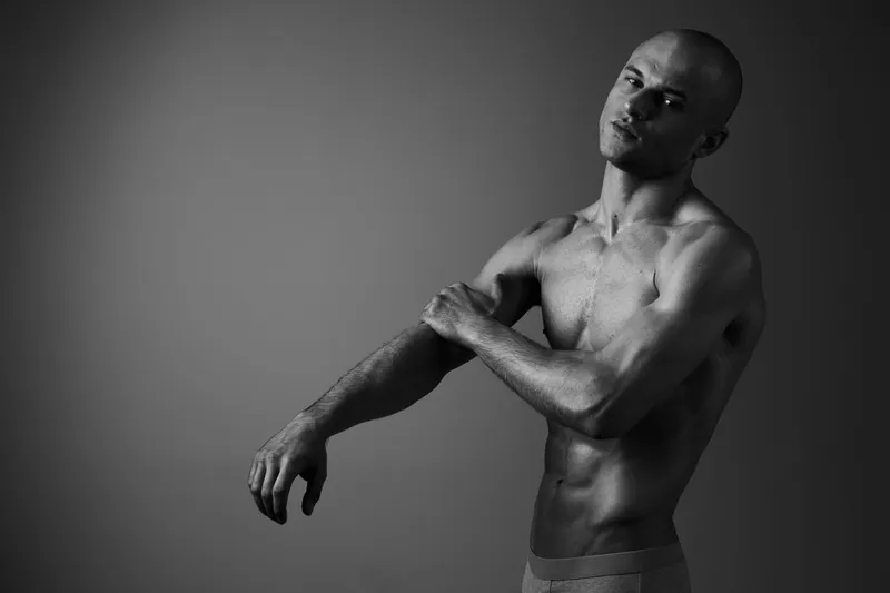 Black and white portrait of a man showcasing strength and confidence, with striking body language and a focused expression emphasizing his physique.