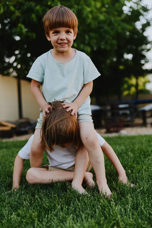 Playful children enjoying their time outdoors, one boy is riding on the back of another, creating a fun and lively atmosphere in the green grass.