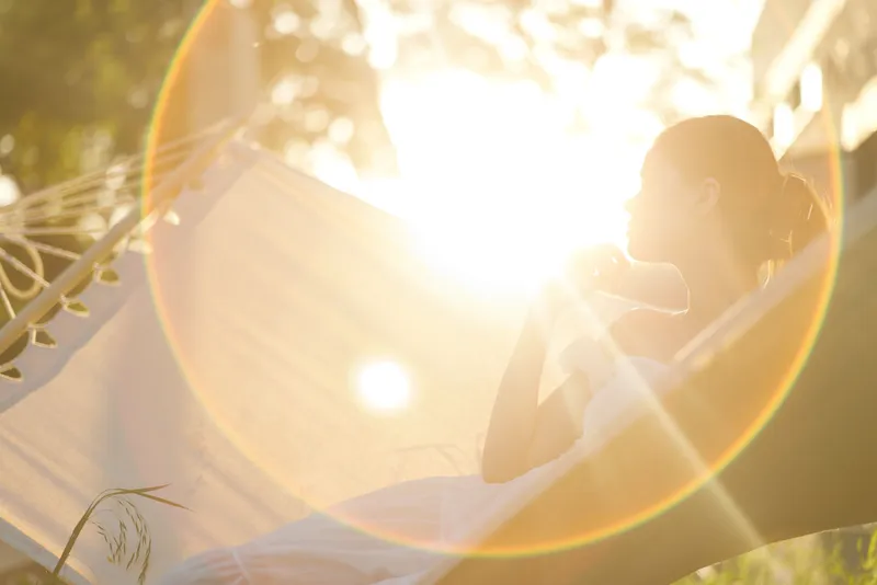 Woman relaxing in a hammock during sunset, enjoying tranquil moments and sunlight, embodying peace, serenity, and natural beauty in a warm atmosphere