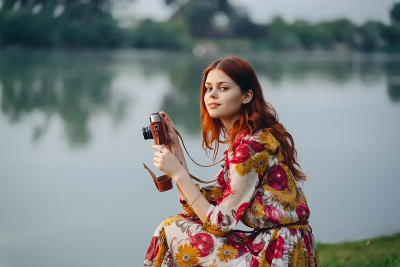 Женщина в разноцветном платье с фотоаппаратом в руках на природе, у реки, хобби