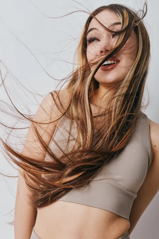 Young woman with long flowing hair posing with closed eyes and smile wearing casual sleeveless top on plain light background. Beauty, happiness, lifestyle and fashion portrait.