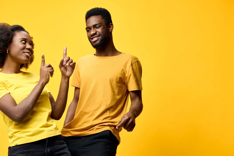Joyful young couple in matching yellow t shirts enjoying a playful moment against a bright yellow background, radiating happiness and positivity