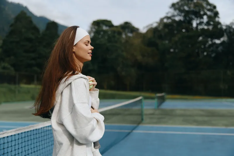 Young woman in sportswear expressing joy on a tennis court, with a serene background, reflecting healthy lifestyle and sports enthusiasm