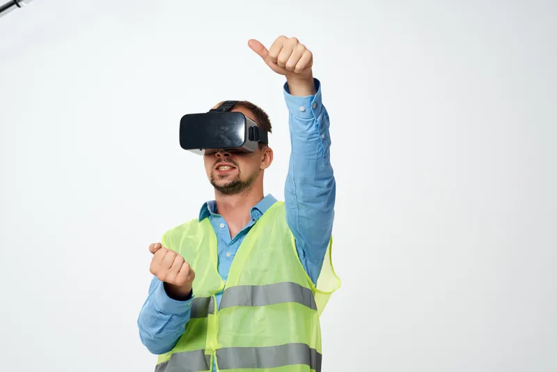 Рабочий в белой каске позирует в студии, используя VR-очки для строительства