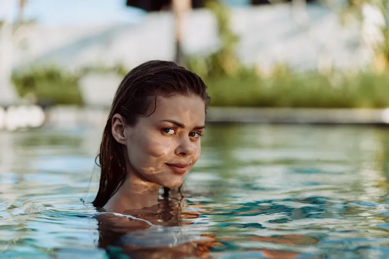 Relaxed woman in a pool outdoors with warm sunlight on her skin, calm expression, enjoying leisure and summer mood in clear water by a tranquil backdrop